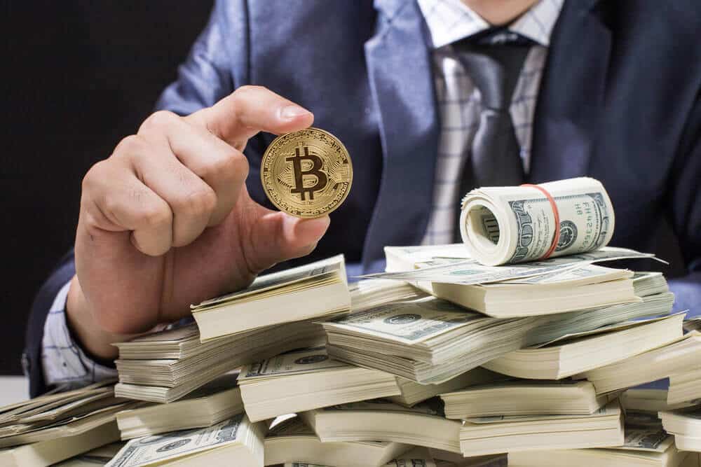 Bitcoin, un empresario sosteniendo una moneda bitcoin y un montón de efectivo debajo de la moneda.