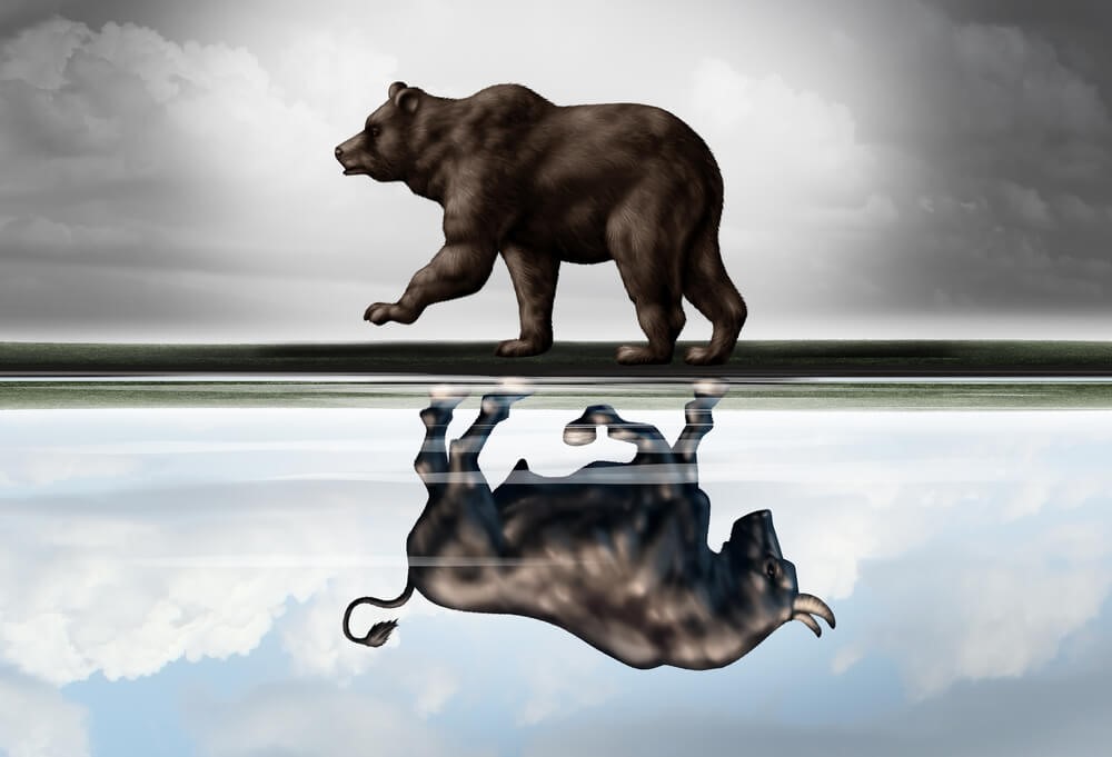 A bull walking on top of a line, a bear walking under it like a reflection.