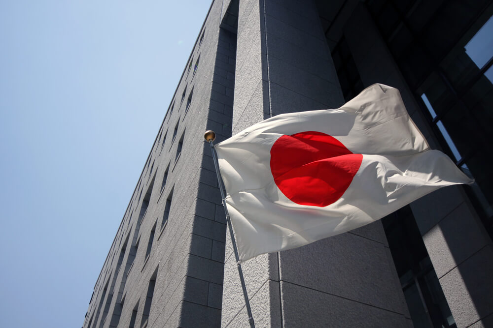 Japanese flag waving in wind in front of building with blue sky